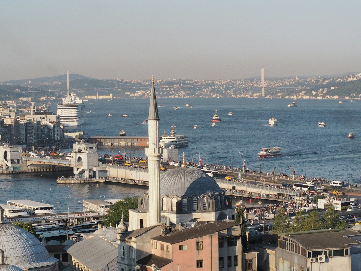 Gemilerin ve köprülerin olduğu hareketli bir su yoluna bakan bir cami.